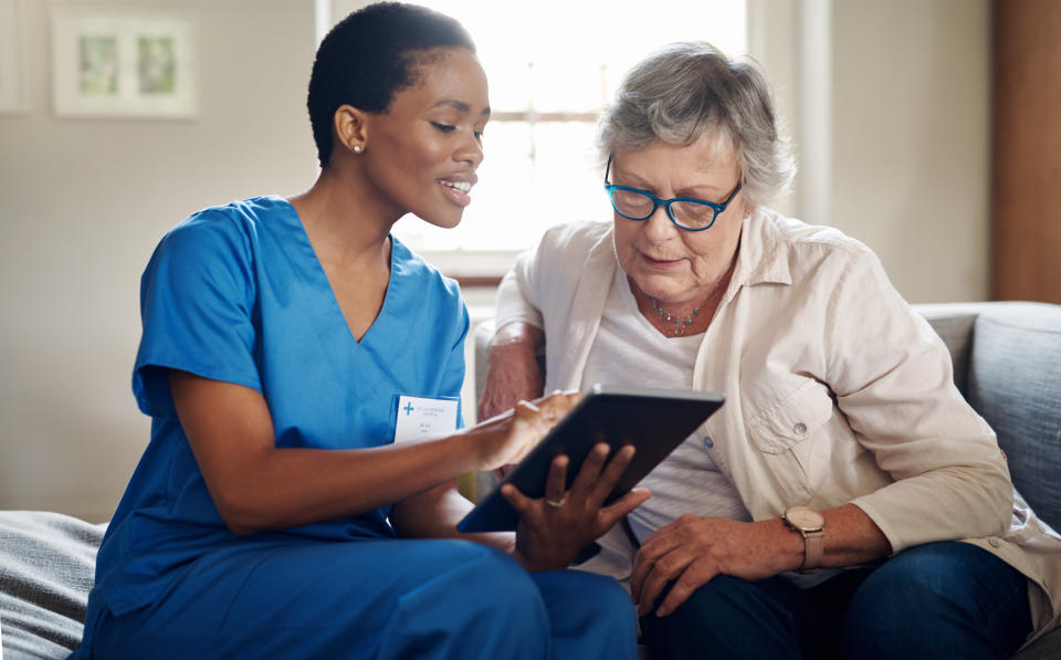 Shot of senior woman using digital tablet with nurse on sofa at home