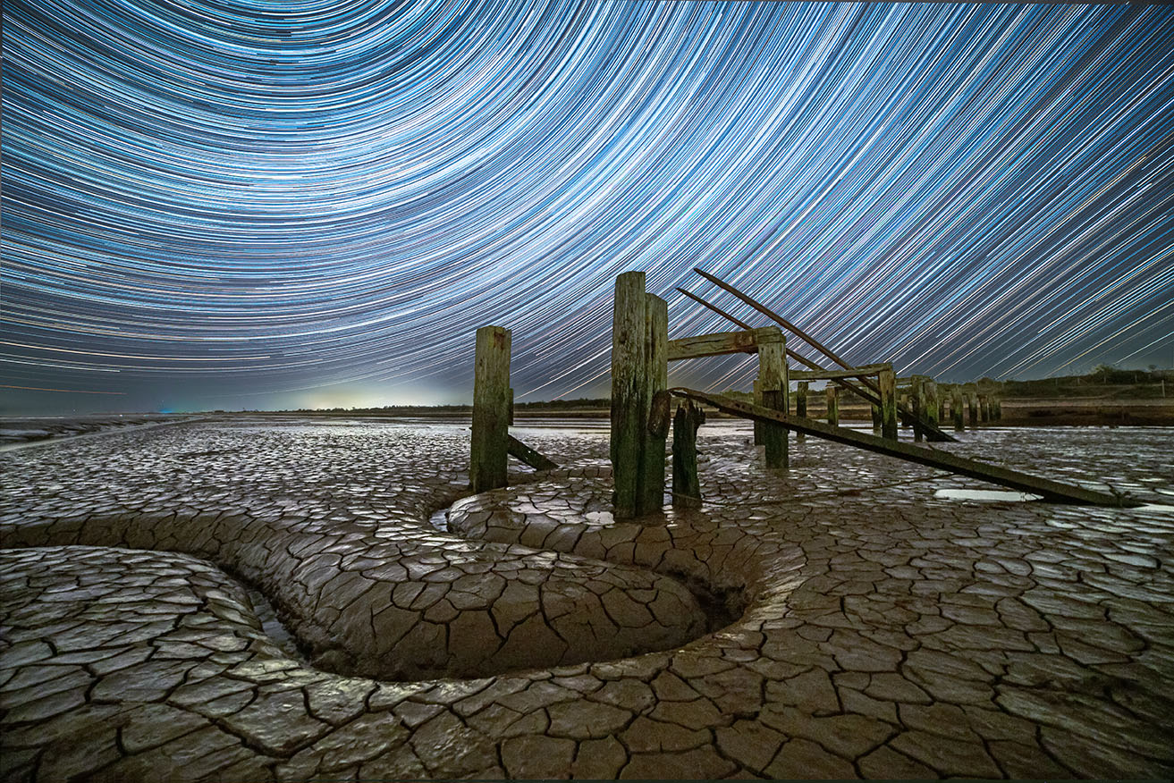 vintage photo of moving stars in the sky shown as streams with a cracked desert in the foreground 