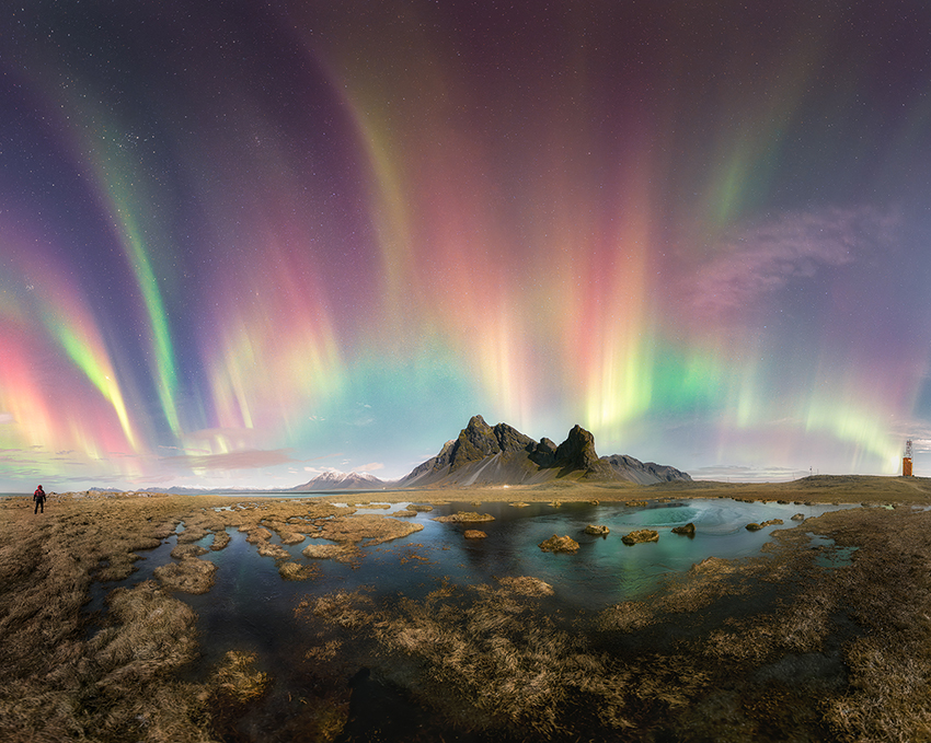 rainbow aurora over the mountain by the lake.  on the left is a person