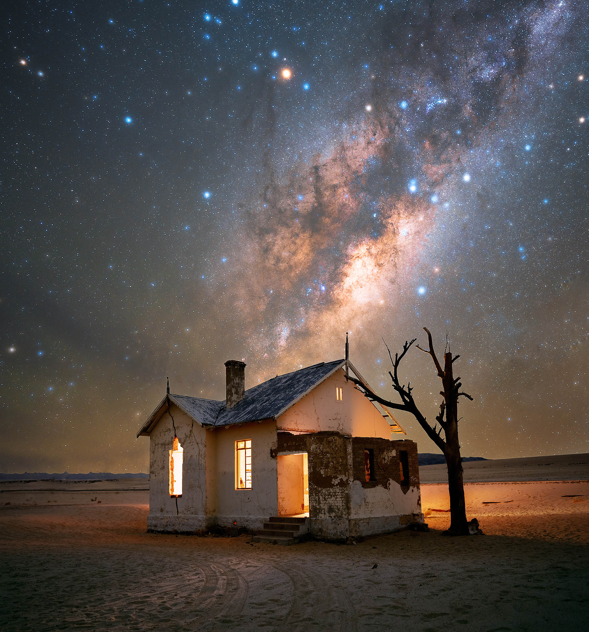 the milky way and thousands of stars above an abandoned house and a dead tree